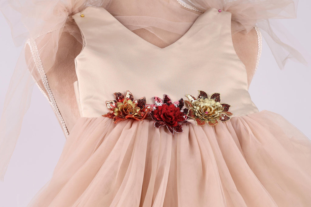 A close-up view of a light pink dress with a v-neck and a full skirt, adorned with three colorful flower embellishments.