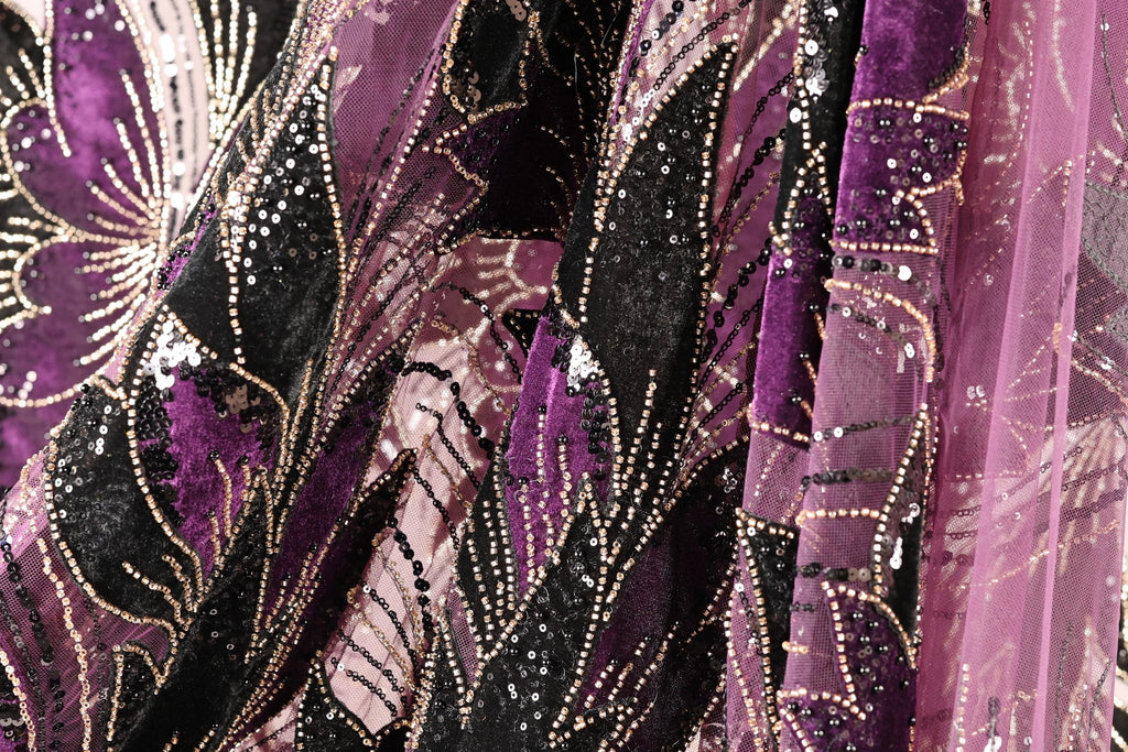 The image is a close-up of a fabric with a floral pattern, featuring a mix of purple and black colors. The fabric appears to be made of a shiny, sequined material, giving it a sparkling and luxurious appearance.