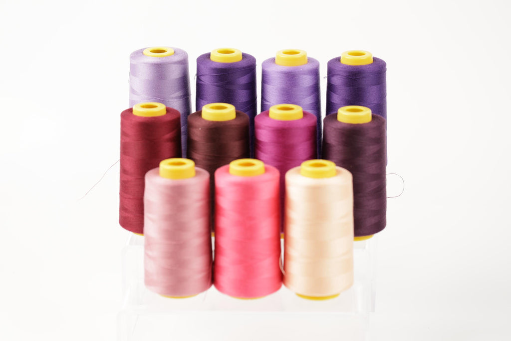 A collection of colorful spools of thread in various shades, including purple, pink, and yellow, arranged in a visually appealing manner.
