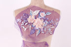A mannequin with a purple fabric draped over its back, featuring a floral design with pink and purple flowers and leaves.
