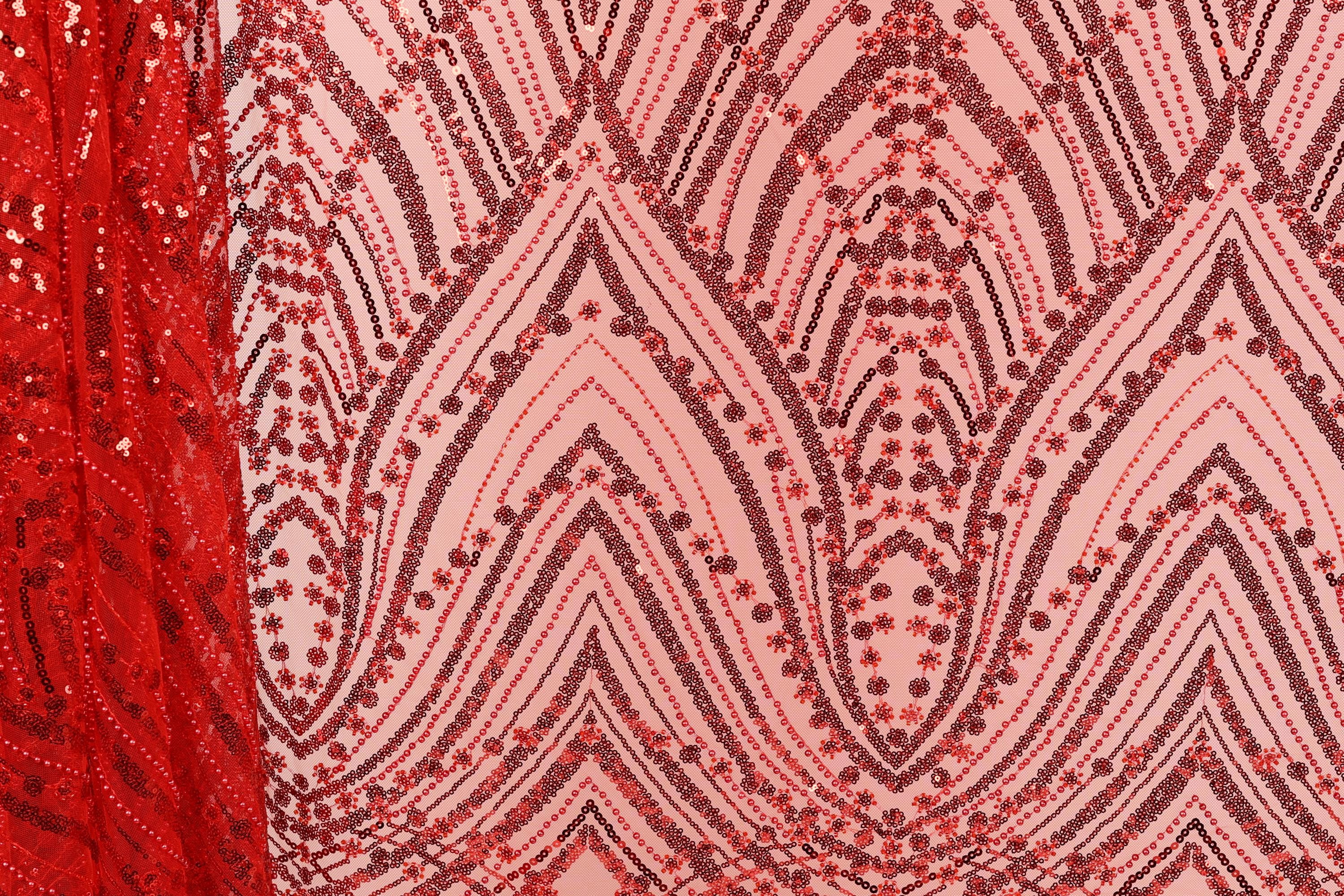 a close-up view of a fabric with a repeating pattern of red and black sequins. The pattern consists of various shapes and designs, creating a visually striking and intricate design.