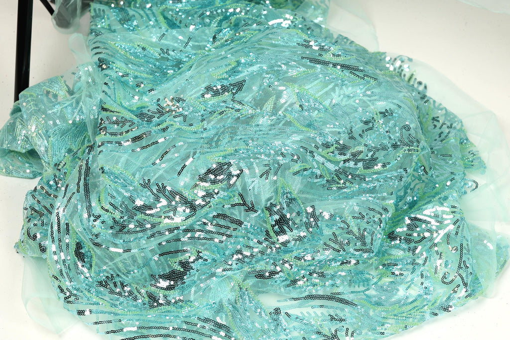 a close-up view of a fabric with a shimmering, sequined texture in shades of blue and green. The fabric appears to be made of a sheer, sheer-like material, giving it a delicate and ethereal appearance.