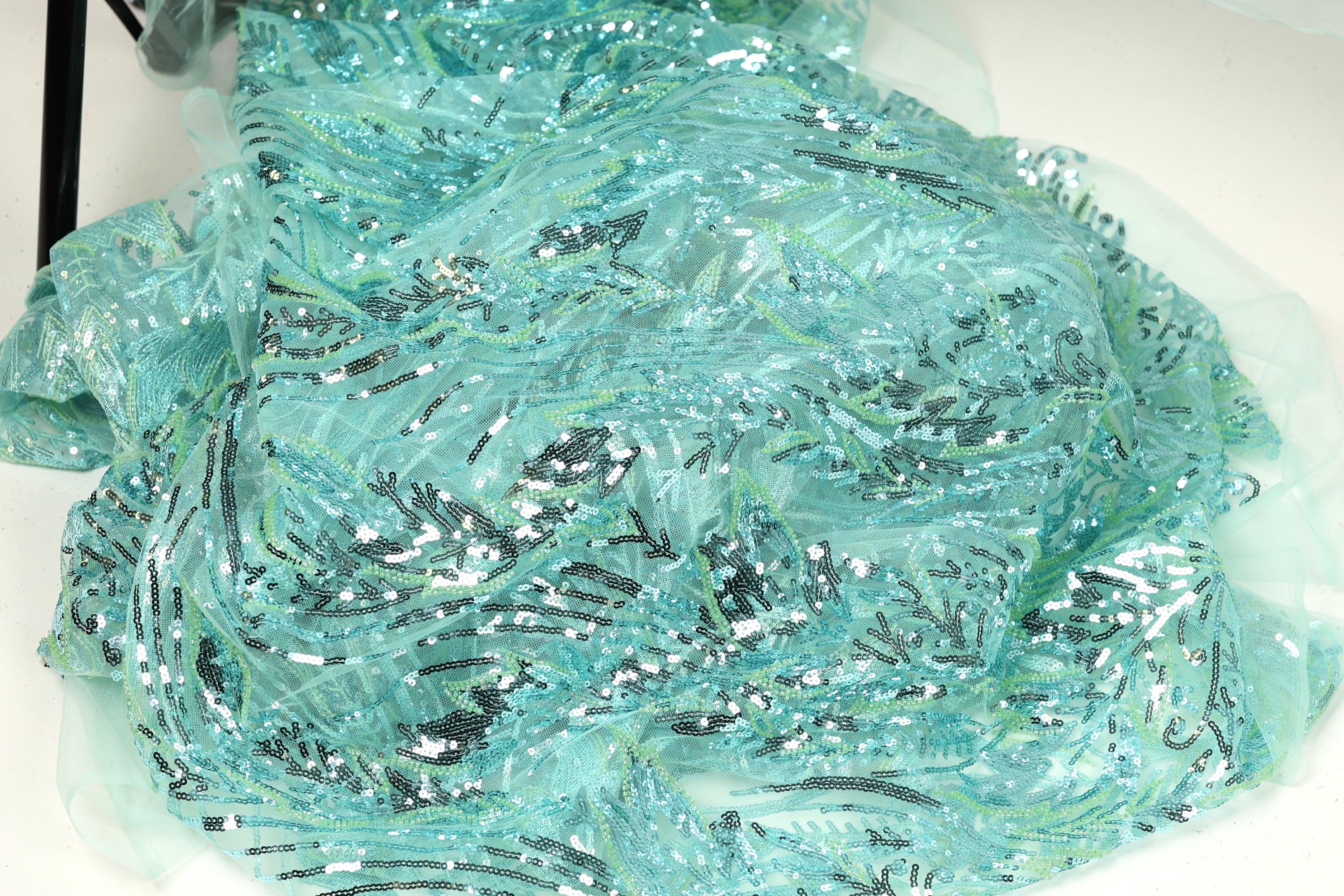 a close-up view of a fabric with a shimmering, sequined texture in shades of blue and green. The fabric appears to be made of a sheer, sheer-like material, giving it a delicate and ethereal appearance.