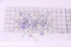 a decorative floral arrangement with purple and white flowers, placed on a transparent ruler against a white background.