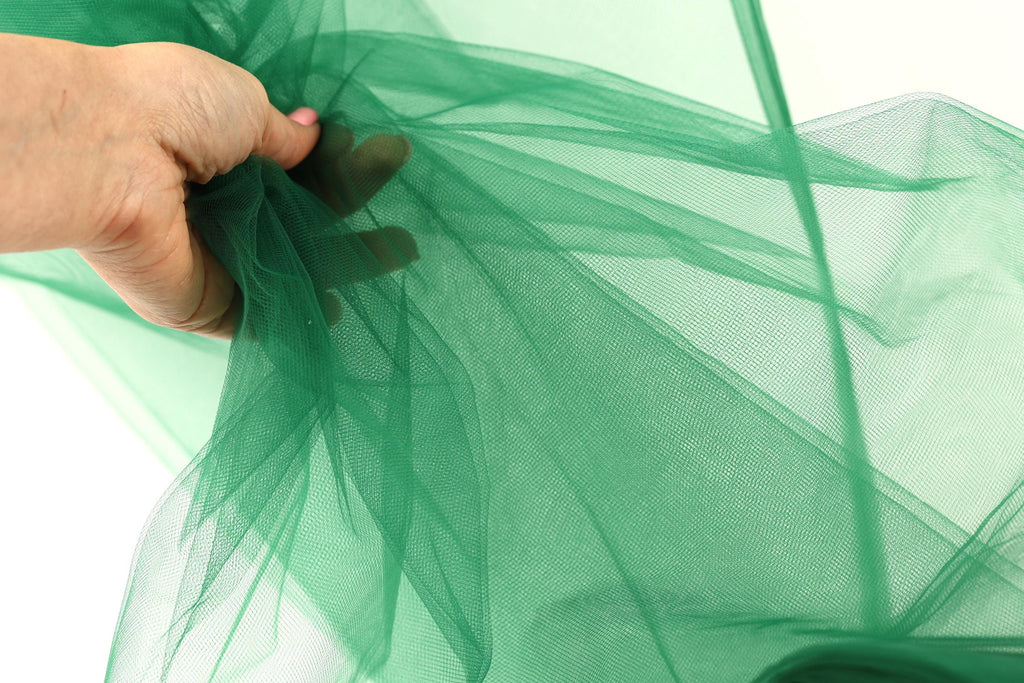 A hand is holding a piece of green tulle fabric, which appears to be a type of tulle material.
