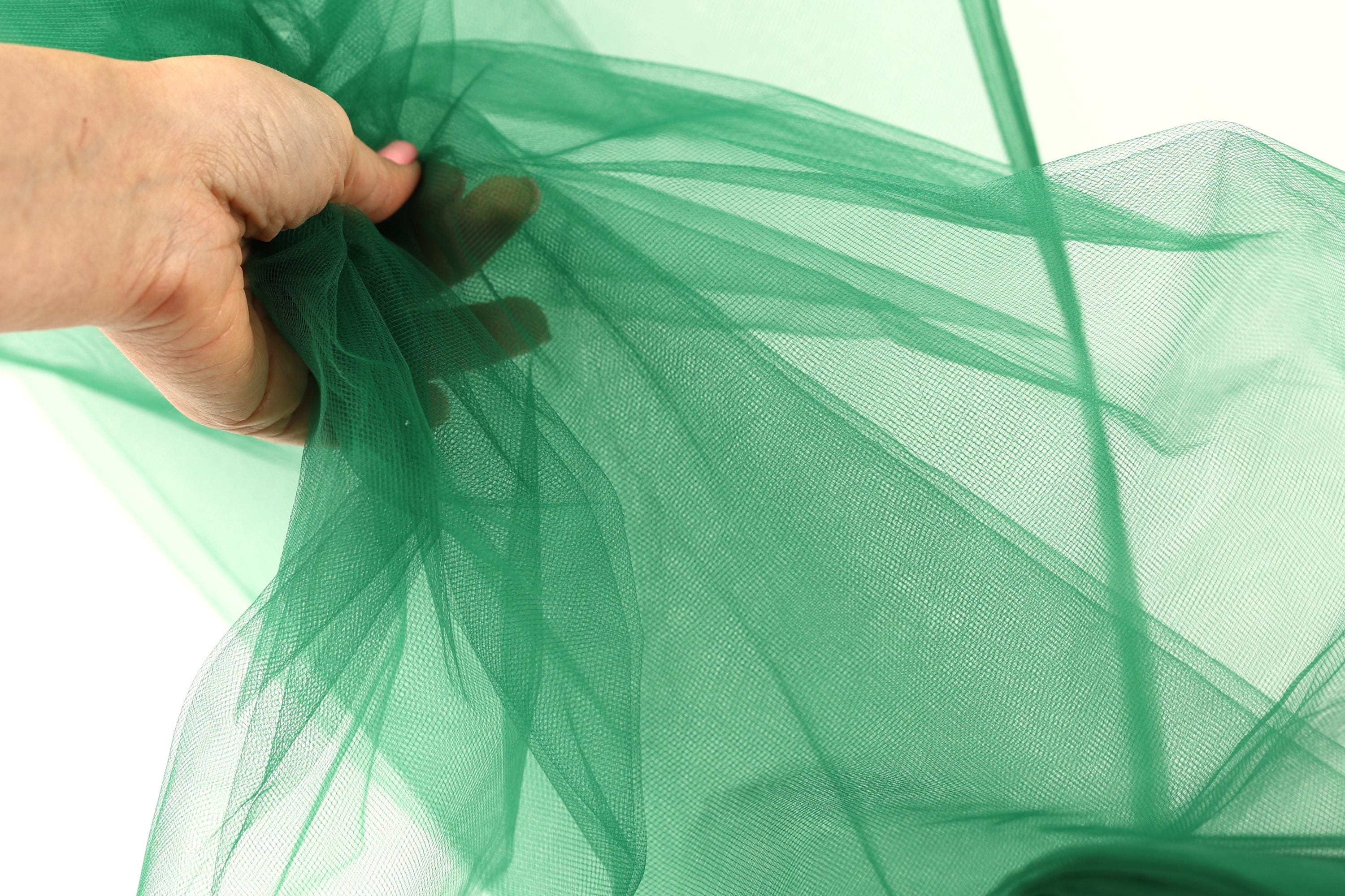 A hand is holding a piece of green tulle fabric, which appears to be a type of tulle material.