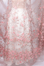 A close-up view of a delicate, white dress adorned with a floral pattern of pink roses. The dress features a sheer, lace-like fabric that adds a soft, romantic touch to the overall design.