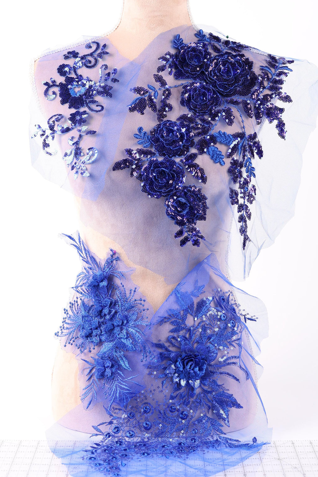 a close-up view of a delicate, intricately designed fabric with a floral pattern in shades of blue and purple. The fabric appears to be a sheer material, with the flowers and leaves appearing to be made of sequins or other embellishments. The overall composition of the image is visually appealing and showcases the craftsmanship involved in creating such a piece of fabric.