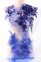 a close-up view of a delicate, intricately designed fabric with a floral pattern in shades of blue and purple. The fabric appears to be a sheer material, with the flowers and leaves appearing to be made of sequins or other embellishments. The overall composition of the image is visually appealing and showcases the craftsmanship involved in creating such a piece of fabric.