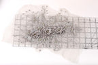 a decorative piece of fabric with a floral pattern, including a variety of flowers and leaves. The fabric appears to be a lace or sheer material, with a metallic or silver-colored appearance. The piece is placed on a transparent ruler, which is lying on a white surface.
