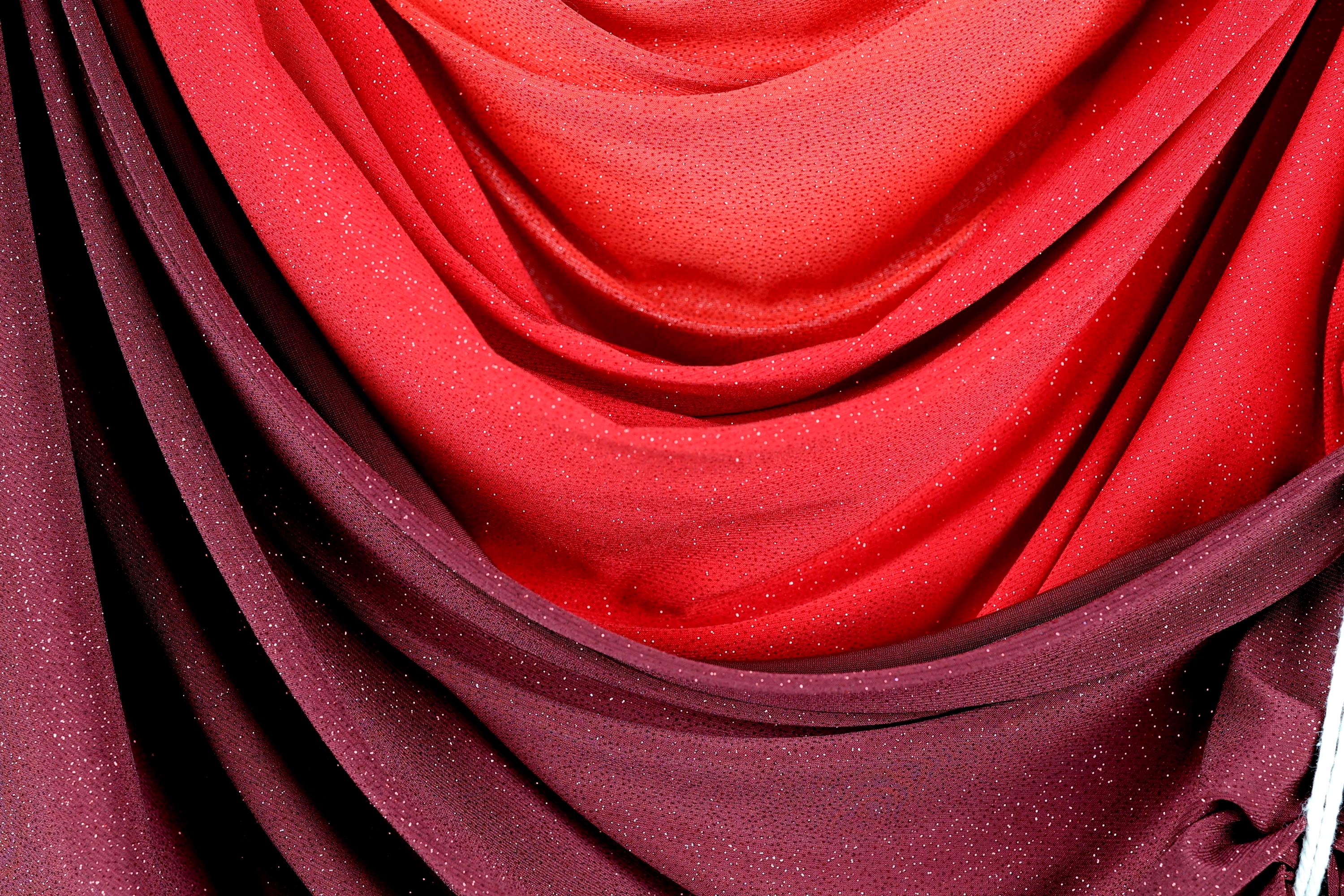 a close-up view of a fabric with a red and purple color scheme, featuring a textured and shiny appearance.