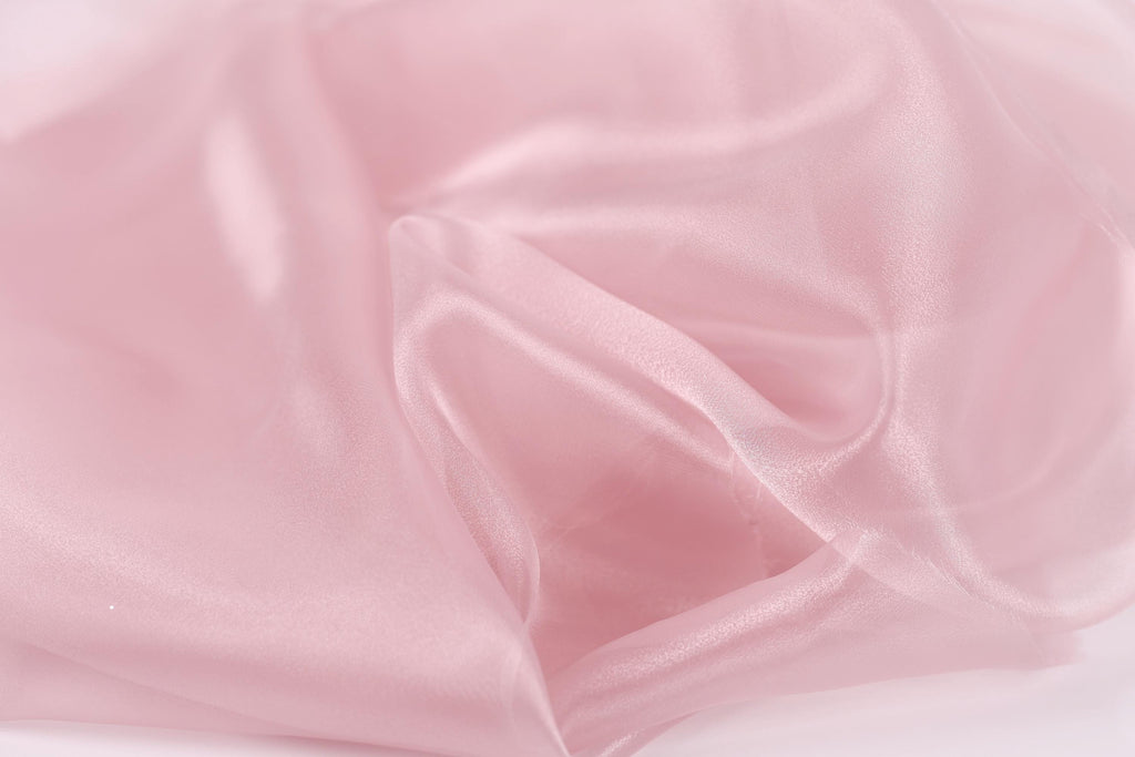 The image is a close-up of a soft, flowing pink fabric, possibly silk or satin, with a smooth and shiny texture.