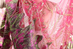 a close-up view of a vibrant, sequined dress with a pink and green color scheme. The dress appears to be made of sheer fabric, giving it a delicate and airy appearance. The intricate patterns and shimmering sequins create a visually striking and eye-catching design.