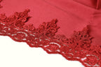 A close-up view of a red fabric with intricate red lace-like patterns along the edge, creating a visually striking and elegant design.