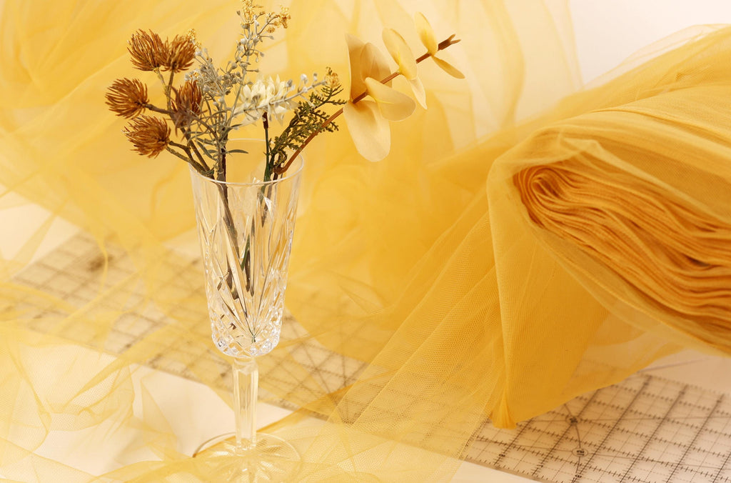 A clear glass vase filled with dried flowers and branches sits on a table covered with yellow fabric.