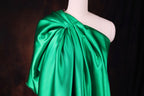 A mannequin wearing a green satin one-shoulder dress with a draped, flowing silhouette.