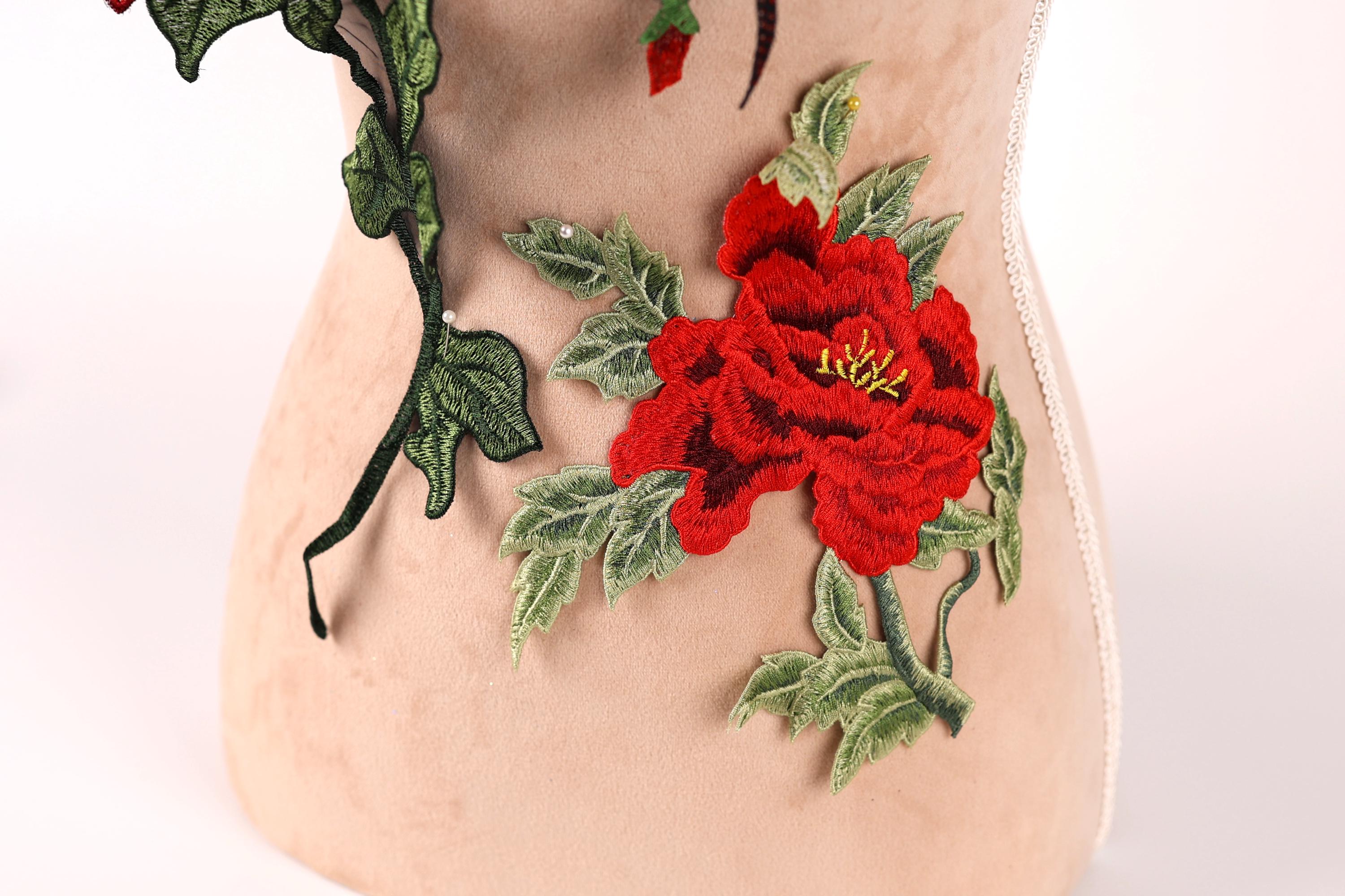 a close-up view of a beige fabric with a vibrant red flower and green leaves as the main focus.