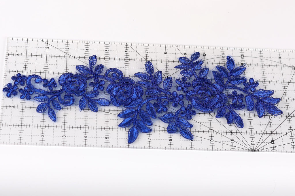 a close-up view of a blue floral embroidery piece on a ruler, showcasing intricate details and patterns.