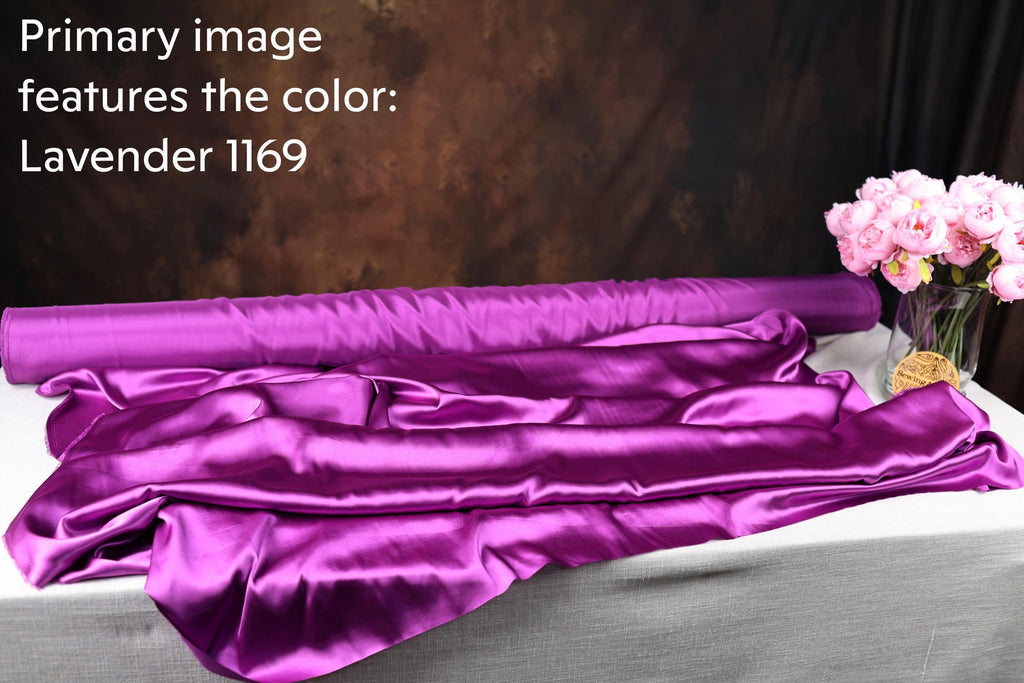 a roll of lavender satin fabric, with a vase of pink flowers placed next to it on a table.