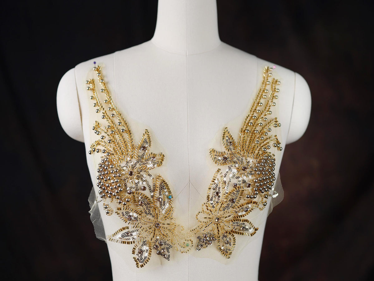 A mannequin wearing a white dress with intricate gold and silver embellishments, including flowers and leaves, on the bust area.