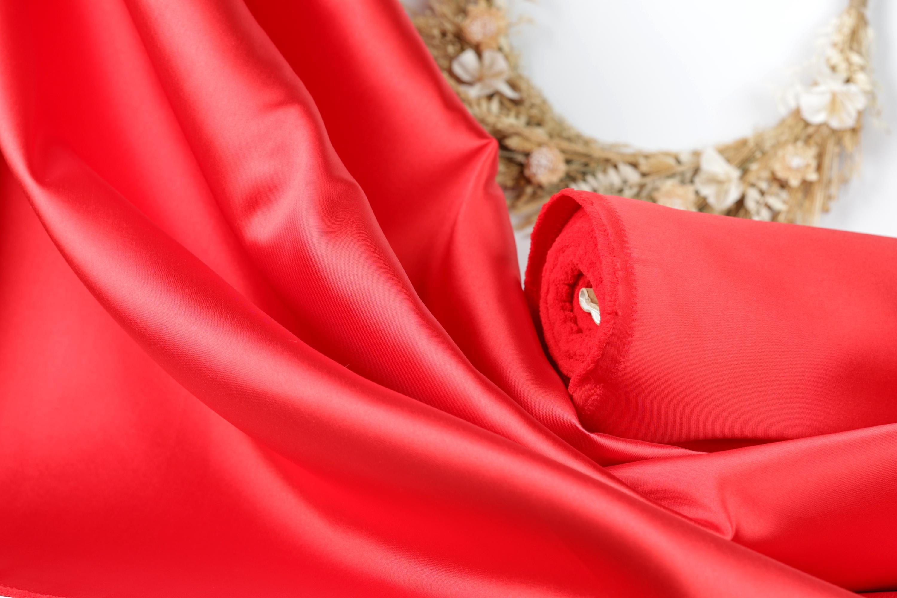 A close-up view of a vibrant red satin fabric, with a wreath of flowers visible in the background.
