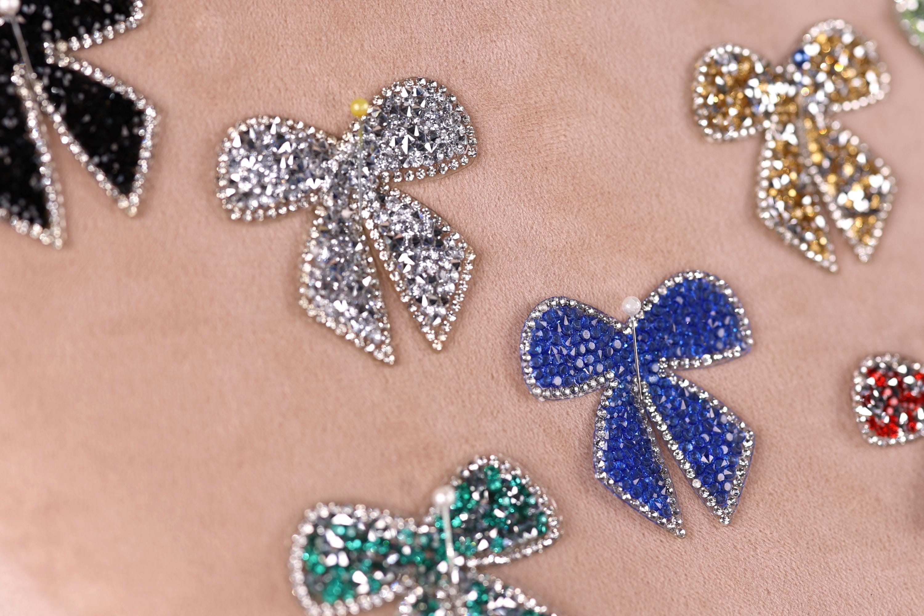 a close-up view of several decorative bow-shaped embellishments, including rhinestones and gemstones, arranged on a light-colored surface.
