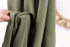 A hand is holding a piece of olive green fabric, which appears to be a type of cloth or textile.