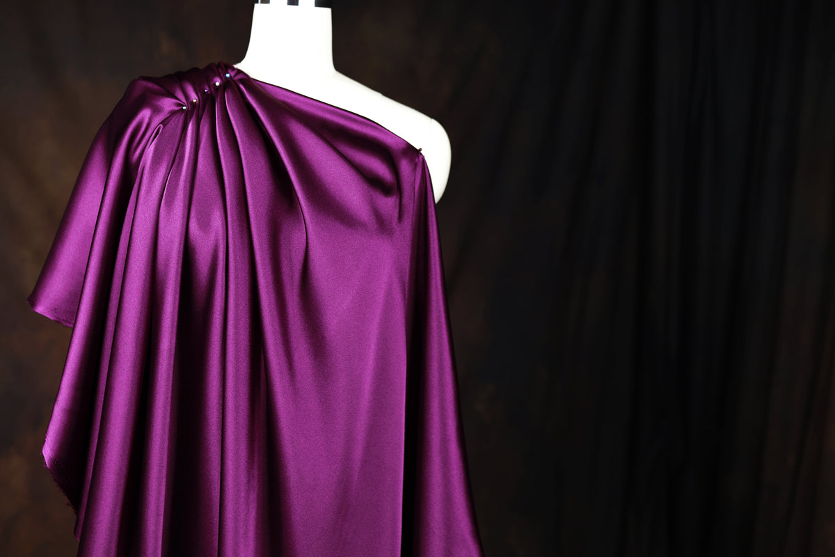 A mannequin wearing a purple satin one-shoulder dress against a dark background.