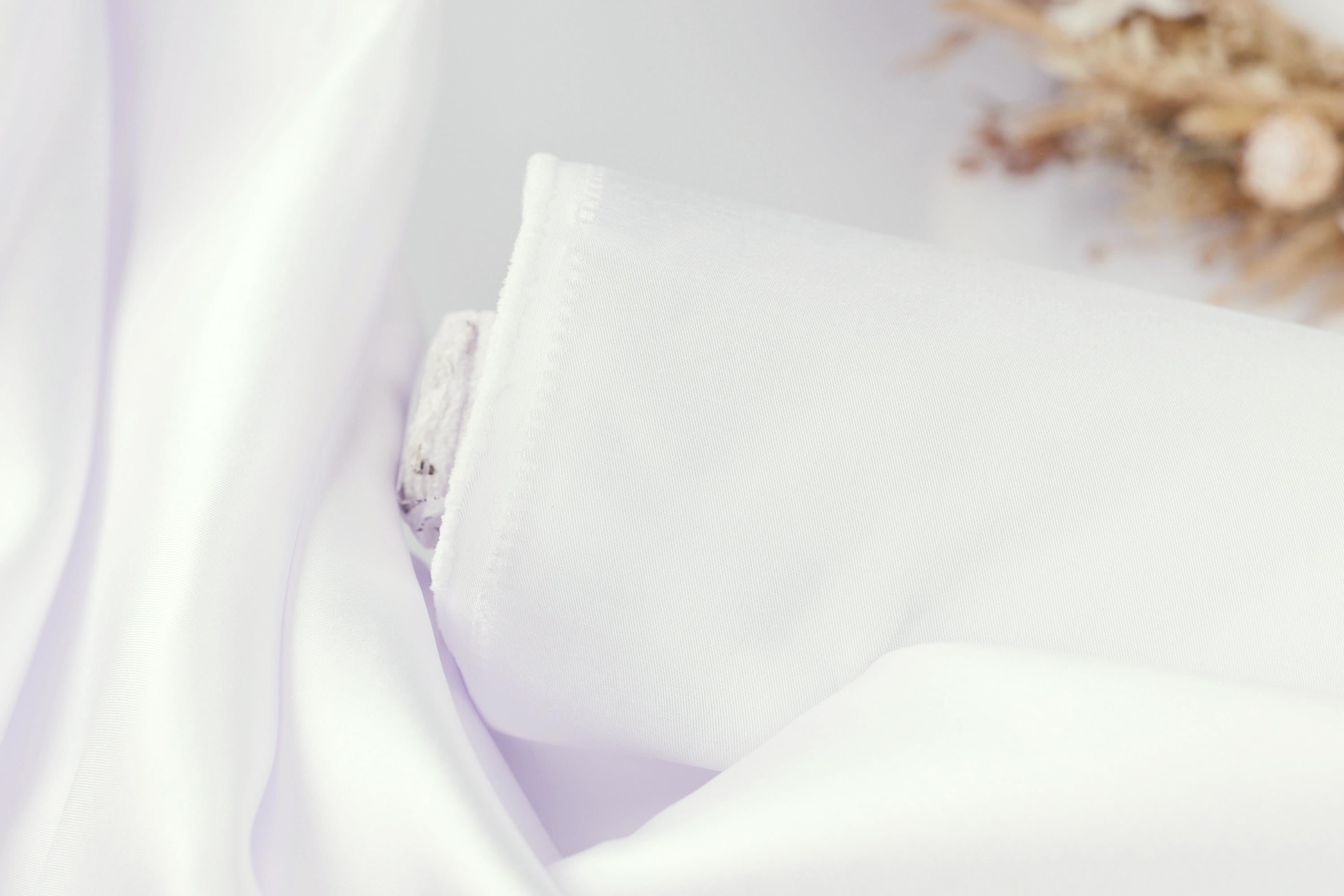A close-up view of a white fabric, possibly a piece of clothing or a sheer curtain, with a blurred background that appears to be a floral arrangement.