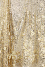 a close-up view of a fabric with a gold and white floral pattern. The fabric appears to be made of a shiny, sequined material, giving it a luxurious and elegant appearance.