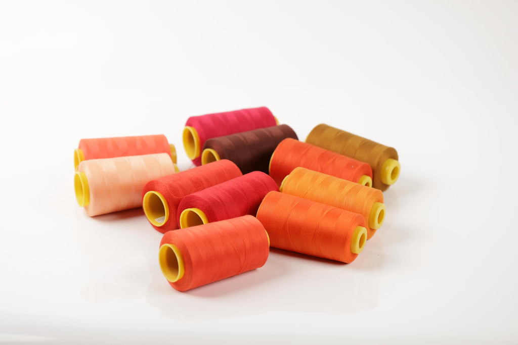 A collection of colorful spools of thread in various shades of orange, red, and brown, arranged on a white background.