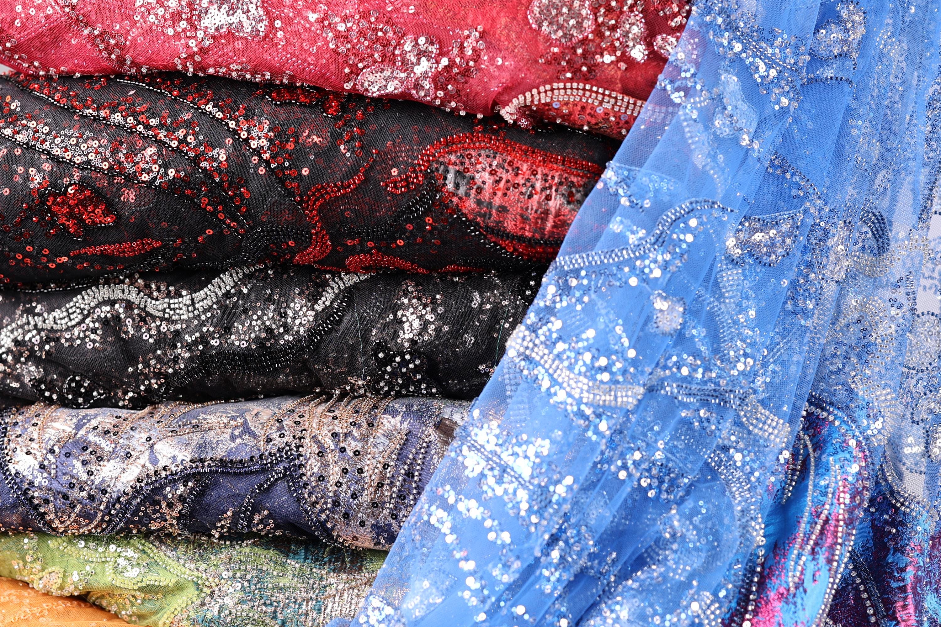 A close-up image of various colorful and patterned fabric swatches, including red, black, blue, and silver sequin designs.