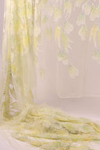a delicate, flowing yellow fabric with a floral pattern, hanging against a plain white background.