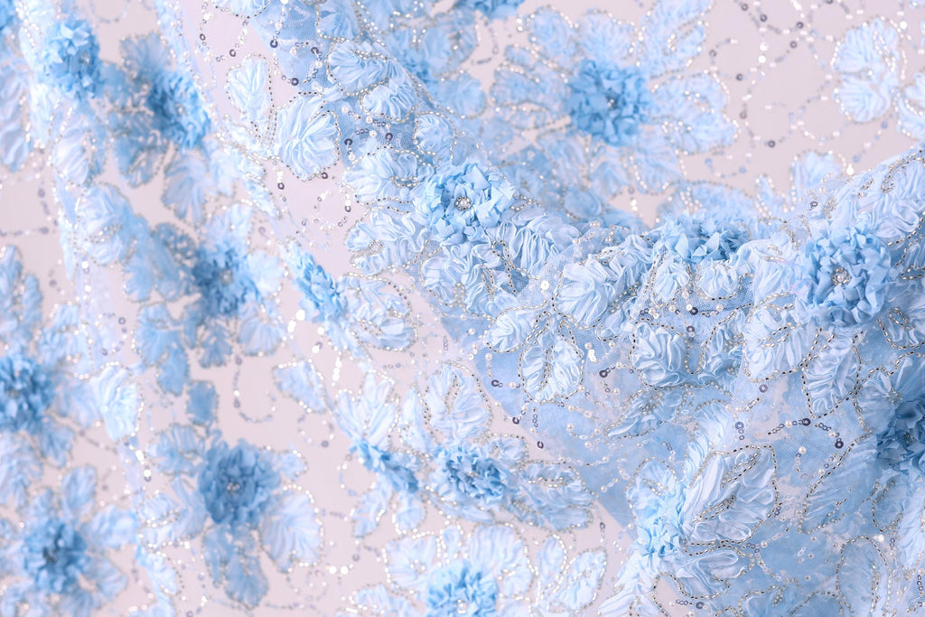 a close-up view of a delicate, intricate fabric with a floral pattern. The fabric is adorned with numerous small blue flowers, each one meticulously crafted and detailed, creating a visually appealing and textured surface. The overall composition of the image is harmonious and balanced, with the flowers and fabric filling the frame and drawing the viewer's attention to their intricate design.