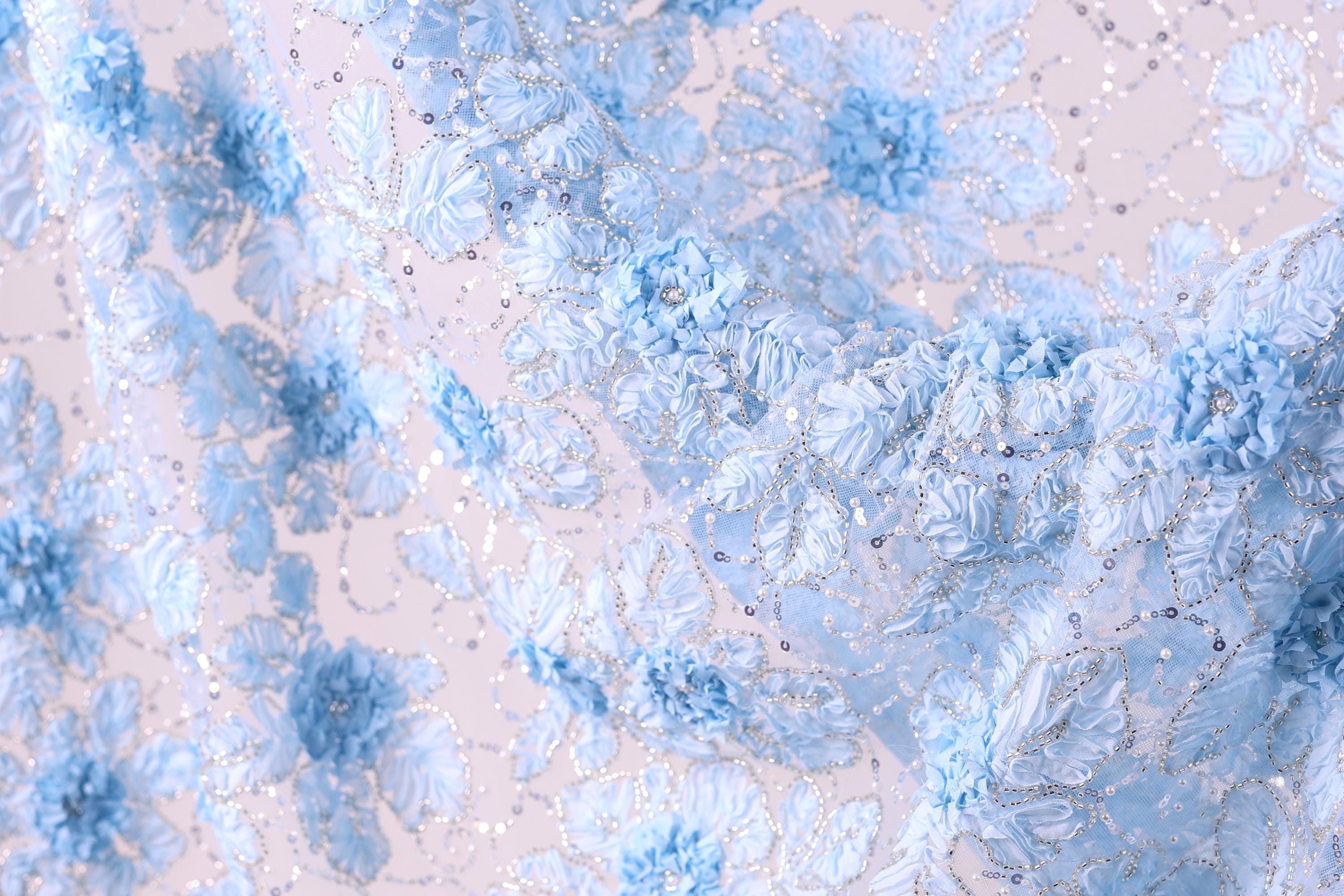 a close-up view of a delicate, intricate fabric with a floral pattern. The fabric is adorned with numerous small blue flowers, each one meticulously crafted and detailed, creating a visually appealing and textured surface. The overall composition of the image is harmonious and balanced, with the flowers and fabric filling the frame and drawing the viewer's attention to their intricate design.