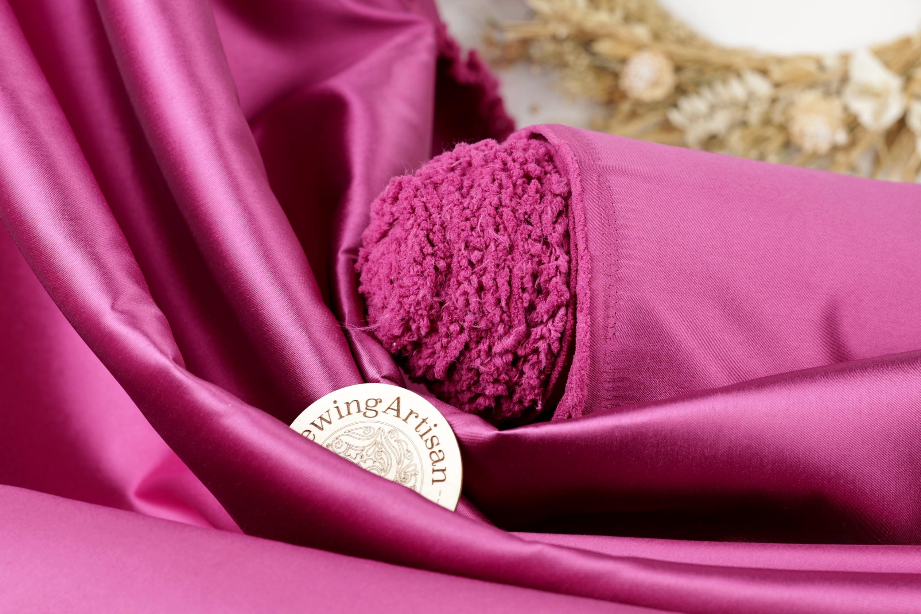 a close-up of a vibrant pink fabric with a small, round, white label that reads "Swing Artisan" placed on top of it.