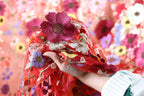 A hand is holding a vibrant red fabric adorned with a large, intricately embroidered flower.