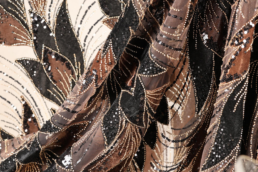 The image is a close-up of a fabric with a floral pattern, featuring a mix of brown, black, and gold colors. The fabric appears to be sequined, with small white beads scattered throughout the design.