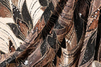 The image is a close-up of a fabric with a floral pattern, featuring a mix of brown, black, and gold colors. The fabric appears to be sequined, with small white beads scattered throughout the design.