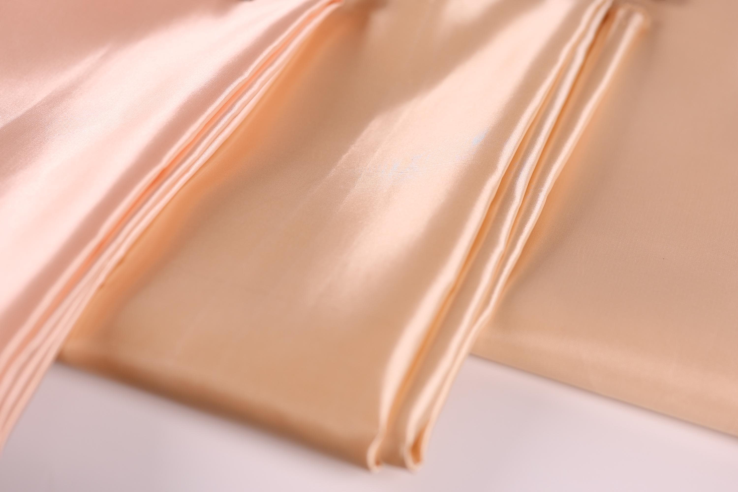 a close-up view of a soft, light peach-colored fabric, possibly silk or satin, with a slightly wrinkled texture.