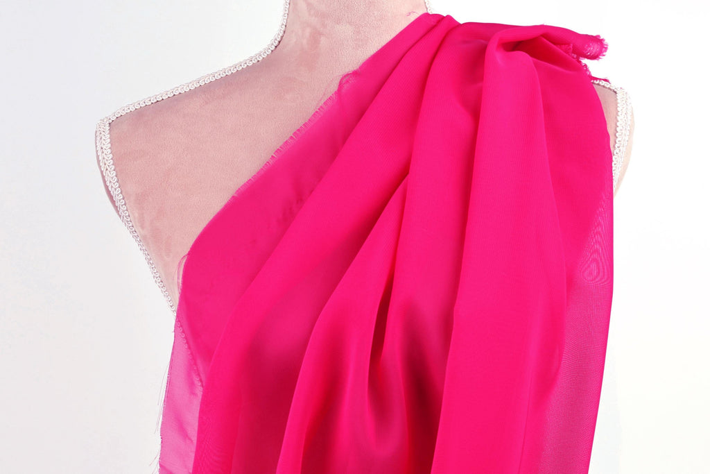 A mannequin wearing a pink, draped fabric draped over its shoulder.