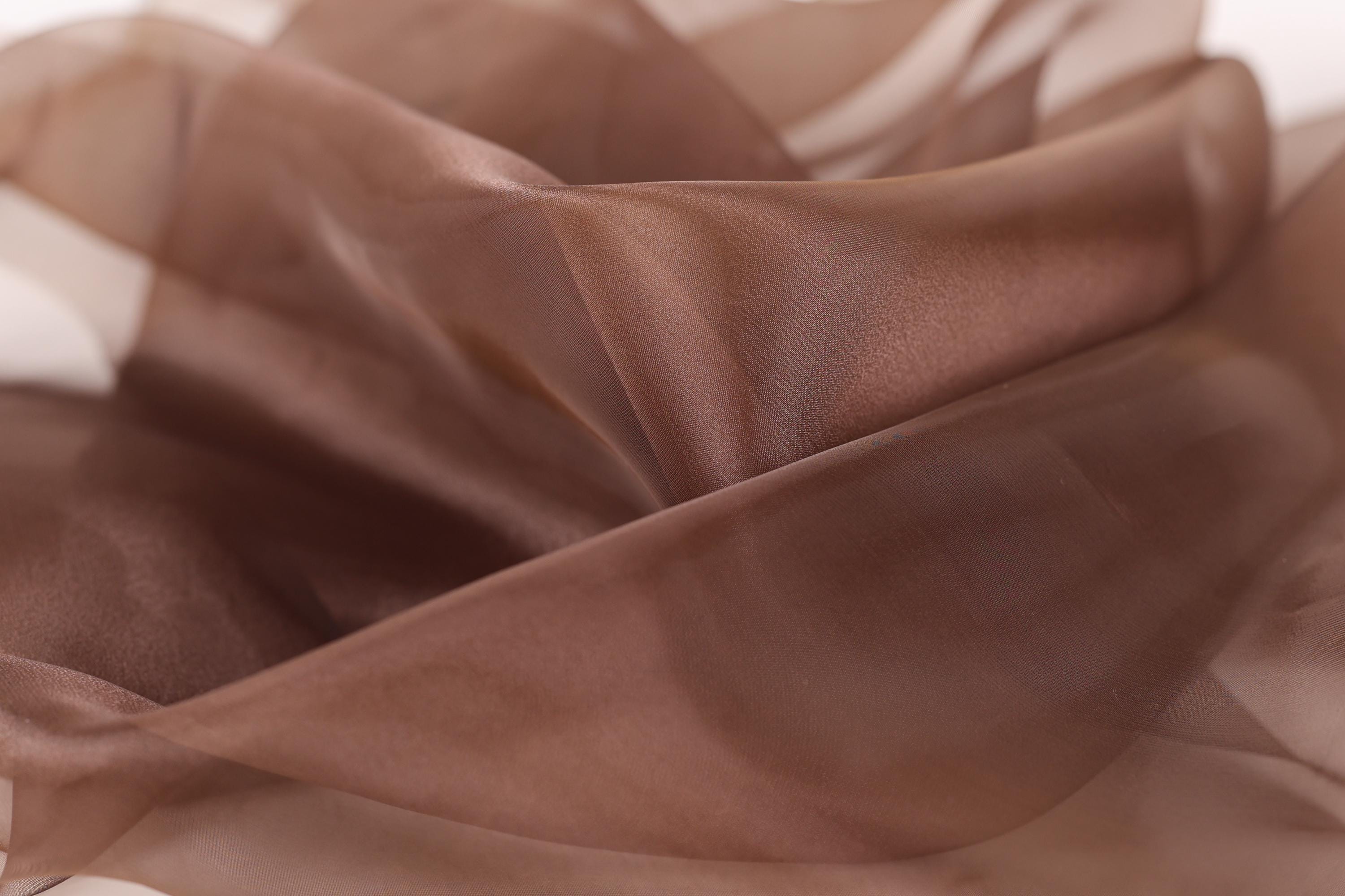 The image is a close-up of a brown fabric, possibly silk or chiffon, with a soft, flowing texture.