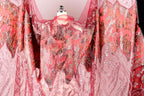 a vibrant, intricately designed dress with a striking pattern of red and pink hues. The dress appears to be made of a sheer fabric, giving it a delicate and airy appearance. The pattern on the dress is quite detailed, with a mix of floral and geometric elements that create a visually captivating design. The dress is displayed on a mannequin, showcasing its unique and eye-catching design.