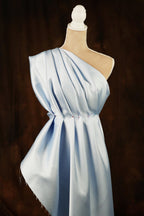 A mannequin wearing a light blue one-shoulder dress with a draped, flowing design.