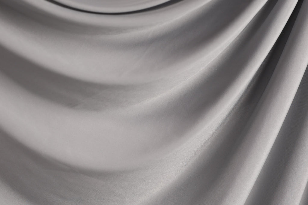 The image is a close-up of a gray fabric, possibly a piece of clothing or a textile. The fabric has a smooth, flowing texture and appears to be made of a soft, shiny material.