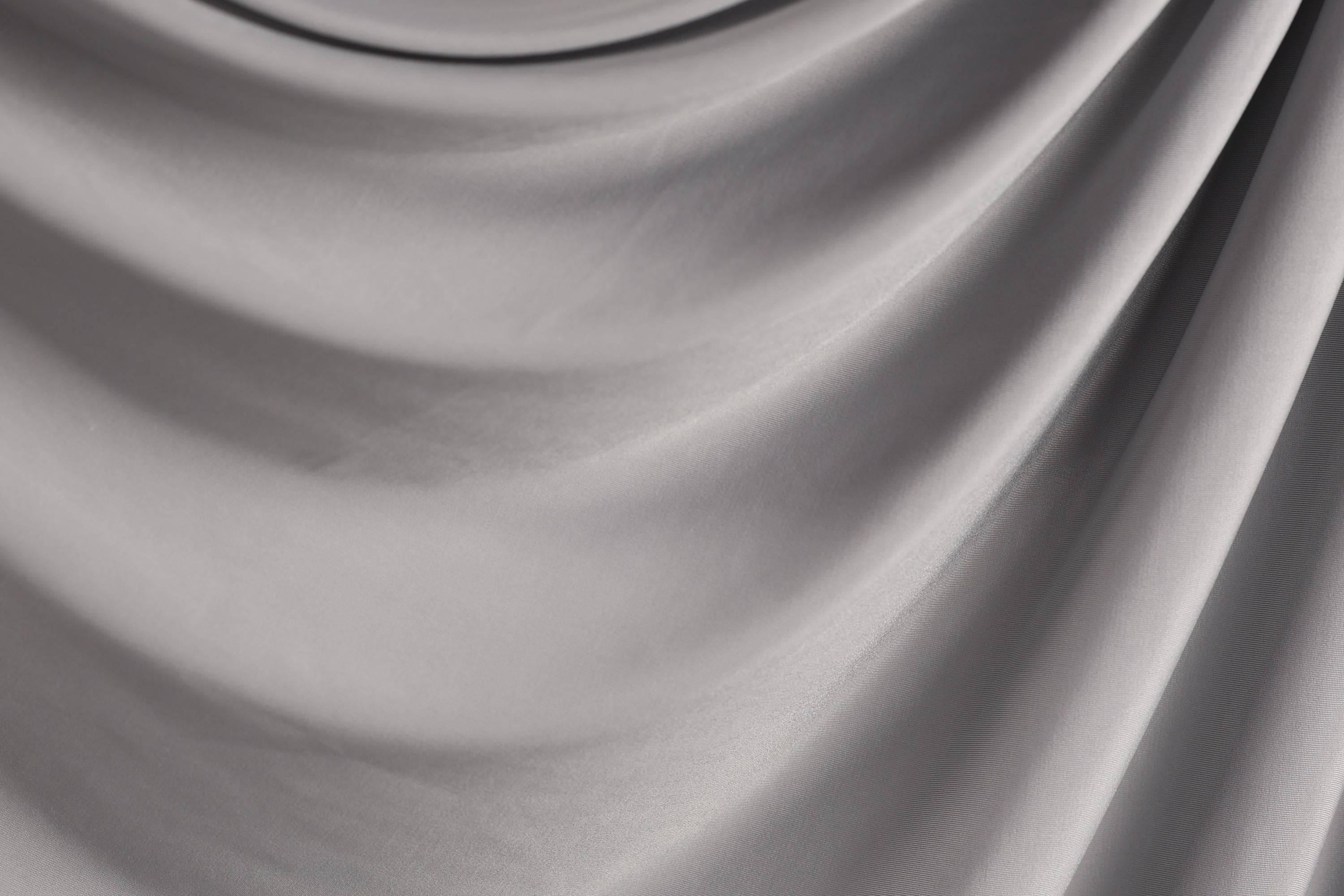 The image is a close-up of a gray fabric, possibly a piece of clothing or a textile. The fabric has a smooth, flowing texture and appears to be made of a soft, shiny material.