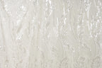 a close-up view of a fabric with a repeating pattern of white and beige lines and shapes, resembling the appearance of grass or leaves.