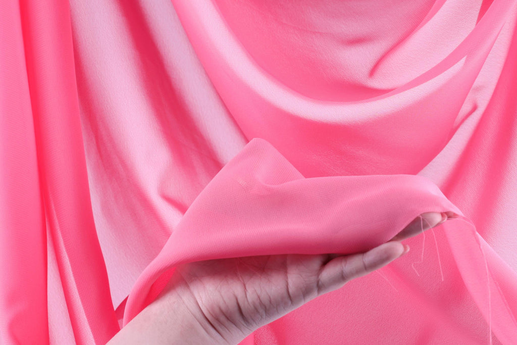 A hand is holding a piece of pink fabric, which appears to be a soft, flowing material.