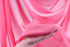 A hand is holding a piece of pink fabric, which appears to be a soft, flowing material.