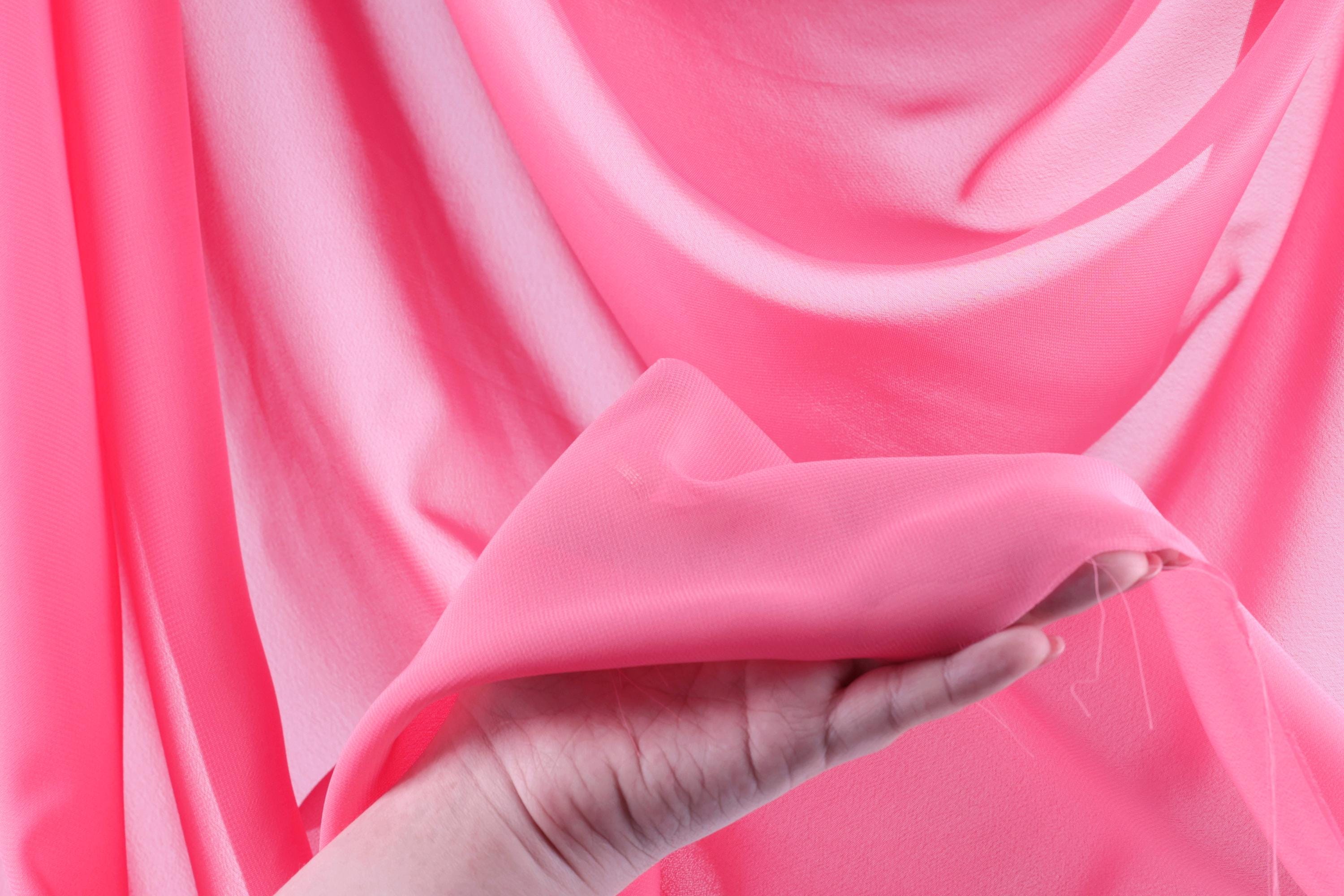 A hand is holding a piece of pink fabric, which appears to be a soft, flowing material.